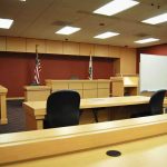 Pop Star’s Alleged Grooming Turns Deadly Interior view of an empty courtroom with wooden furniture and American flags