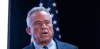 RFK Jr. Sparks Autism Safety Shake-Up Man holding microphone, speaking with American flag behind.