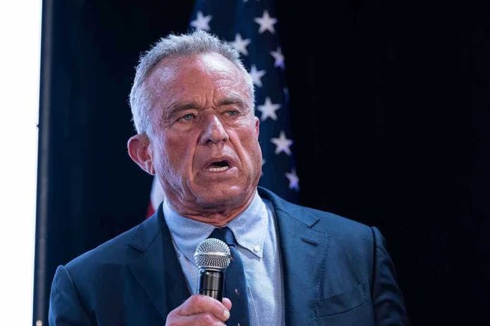 2456684675-1 Man holding microphone, speaking with American flag behind.