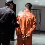 Police officer escorting handcuffed inmate in orange jumpsuit