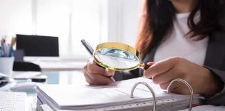 The Mass Shooting Number Game Person using a magnifying glass to review documents in a binder