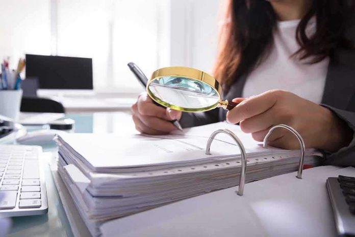 shutterstock_1037672128 Person using a magnifying glass to review documents in a binder