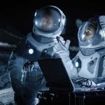 Space Medal Shock — Artemis Crew Elevated Two astronauts in spacesuits review data on a laptop on a moonlike surface at night