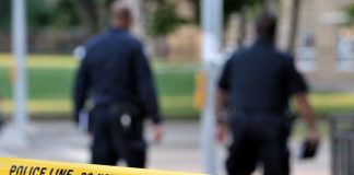 Burglar Shot — Then Drops $10M Bomb Police officers walking past caution tape at a crime scene