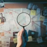 Online Death Threats—FBI Moves Fast Hand holding magnifying glass over investigation board