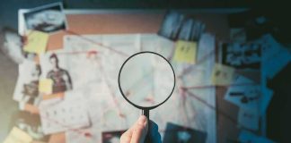 Hand holding magnifying glass over investigation board