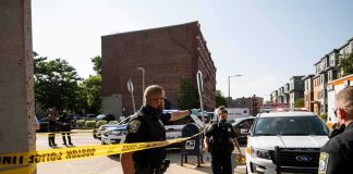 Police officers secure an urban street with yellow tape near patrol cars