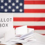Ballot box with papers in front of an American flag