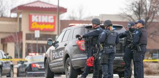 Police officers gather beside a patrol SUV at a taped-off scene