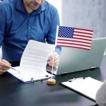 Six-Figure Bribes To Keep Military Members Two people at a desk reviewing documents with a small American flag by a laptop