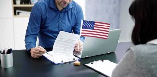 Six-Figure Bribes To Keep Military Members Two people at a desk reviewing documents with a small American flag by a laptop