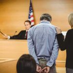 Trusted Army Insider Runs $266K Scam Defendant in handcuffs stands before a judge in a courtroom