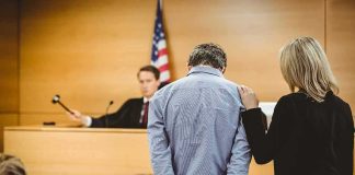 Defendant in handcuffs stands before a judge in a courtroom