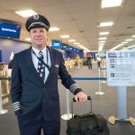 Airline pilot standing in airport check-in area with rolling bag