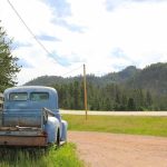 Old blue pickup truck parked by a rural dirt road