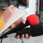 DOJ Hit Job? Newsom Drops Bomb Journalist holding two microphones while writing in a notebook