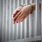 handcuffed hands resting through prison bars