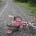 Pink children's bicycle with training wheels lying on a gravel path