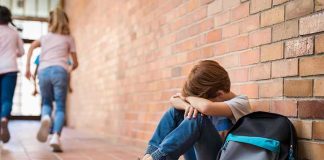 boy sitting against brick wall with head on arms and backpack