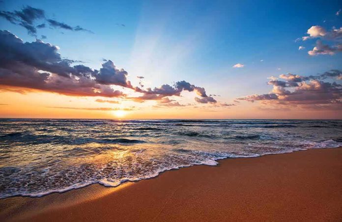 shutterstock_1196505853 sunset over ocean waves on sandy beach