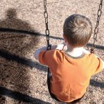 Pregnant Cop Fights Off Child Abductor A young boy sitting on a swing at a playground, with his shadow cast on the ground