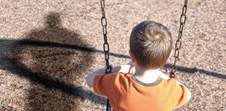 Pregnant Cop Fights Off Child Abductor A young boy sitting on a swing at a playground, with his shadow cast on the ground