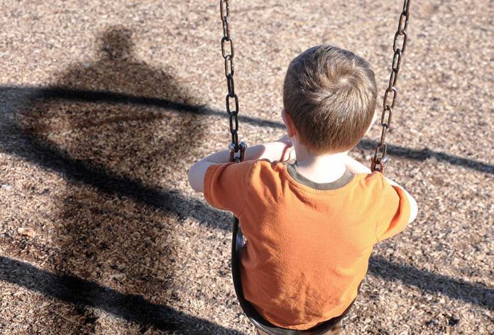 shutterstock_121428757 A young boy sitting on a swing at a playground, with his shadow cast on the ground