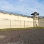 Prison Bloodbath- Two-Day Carnage Prison yard with chain-link fence and guard tower