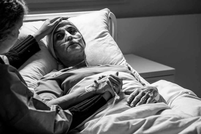 Patient in hospital bed with nasal oxygen held by visitor