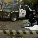 Crime scene with police car and two investigators by a covered body