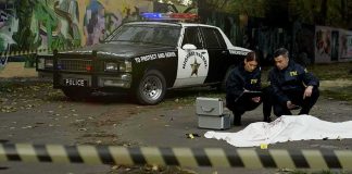 Crime scene with police car and two investigators by a covered body