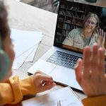 Student in headphones waving at a person on a laptop video call