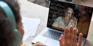 Student in headphones waving at a person on a laptop video call