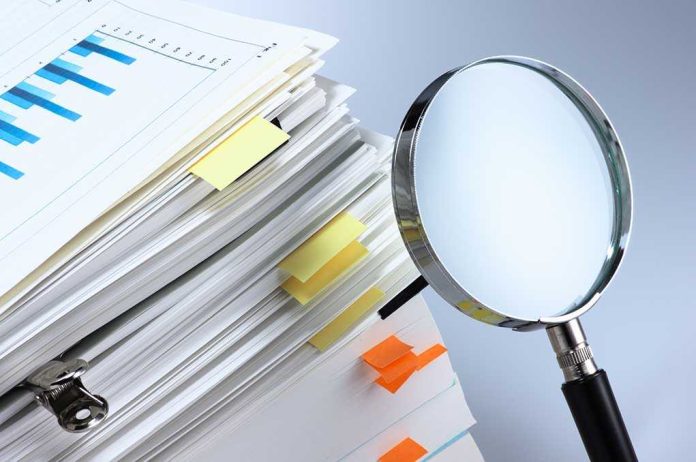 shutterstock_174064394 Stack of documents with a magnifying glass beside it