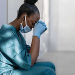 Rugby Star’s Career Wrecked—Doctor’s Advice Backfires Healthcare worker in scrubs sitting against a wall with head bowed