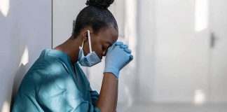 Healthcare worker in scrubs sitting against a wall with head bowed