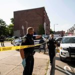 Holiday Chaos Explodes: Officer Dragged, Guns Found Police officers secure an urban street with yellow tape near patrol cars