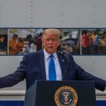 Hormuz Flashpoint: 80 Targets Hammered Donald Trump speaks at a podium with arms outstretched