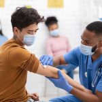 Healthcare worker gives vaccination to masked patient in clinic