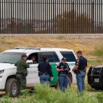 Body-Cam Blackout Sparks ICE Firestorm law enforcement officers confer beside patrol vehicles near a border fence