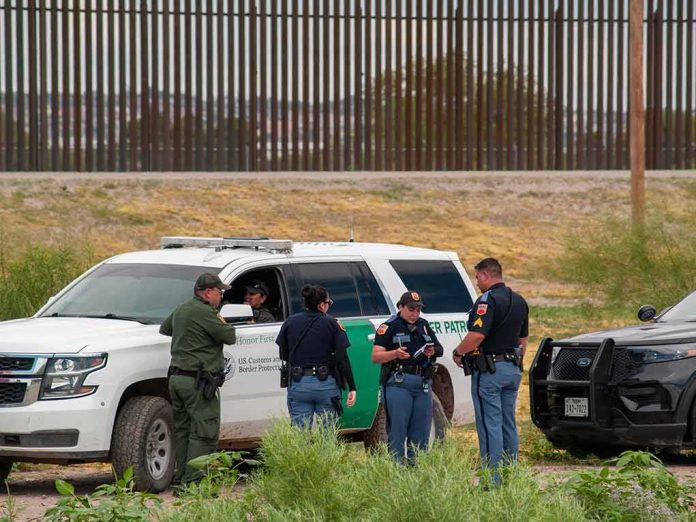law enforcement officers confer beside patrol vehicles near a border fence