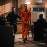 Defendant in orange jumpsuit escorted by officer in courtroom