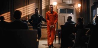 Defendant in orange jumpsuit escorted by officer in courtroom