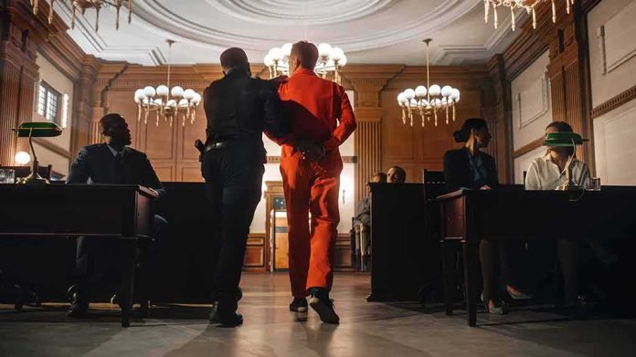 shutterstock_2056444886 Prisoner in orange jumpsuit escorted by officer in a courtroom