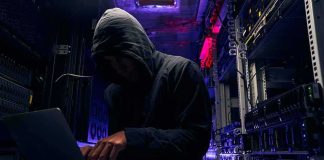 Hooded person using a laptop in a dark server room