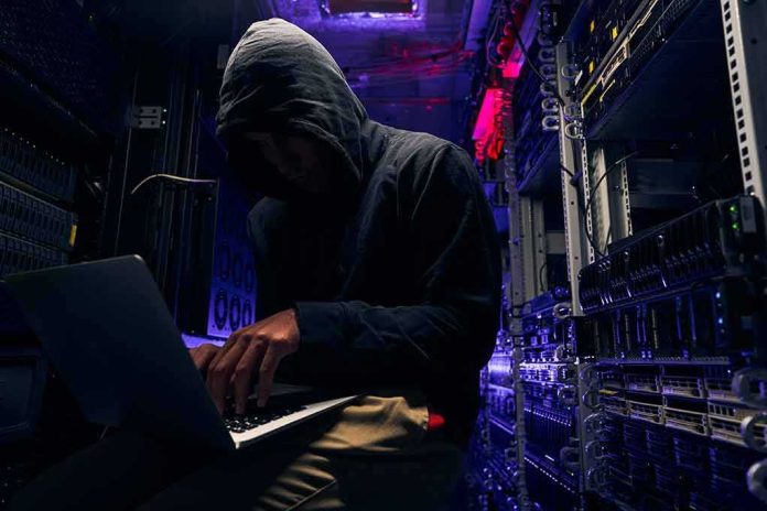 Hooded person using a laptop in a dark server room
