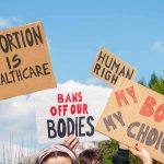 Men Pregnant? Congress Clip Ignites Firestorm Protesters hold cardboard signs at a rally outdoors
