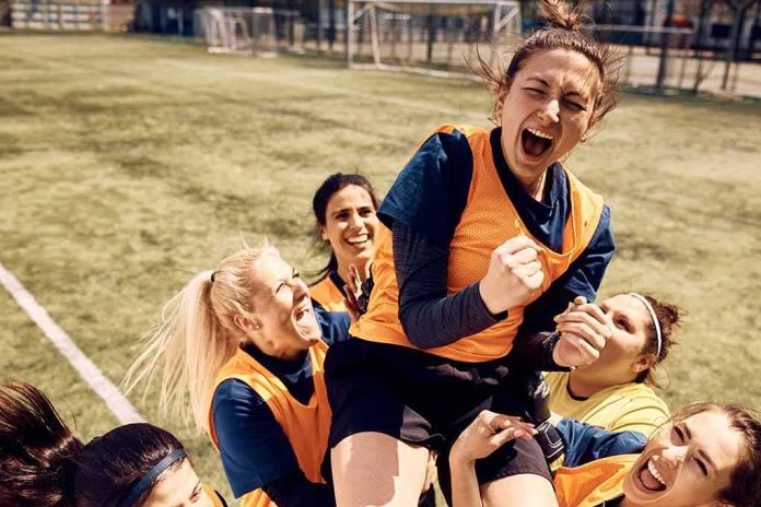 shutterstock_2157299721 Women's soccer teammates celebrate lifting a player