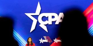 Woman in red speaks at podium on brightly lit conference stage