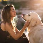 Woman petting a golden retriever at sunset
